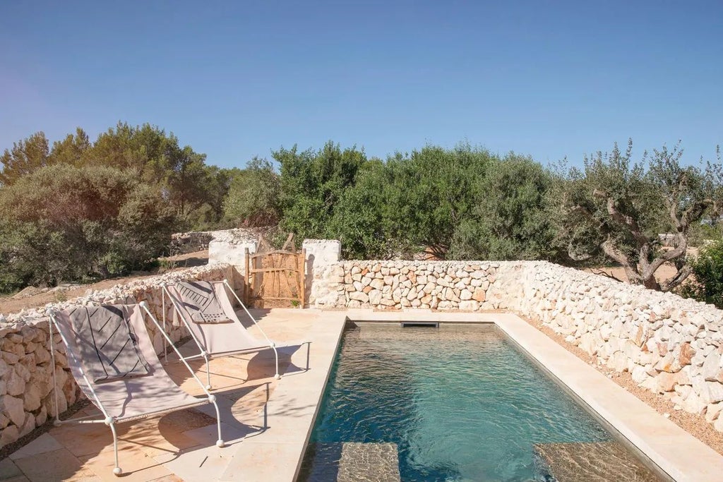 Luxurious whitewashed Mediterranean hotel with stone walls, rustic wooden furniture, and lush greenery overlooking scenic coastal landscape in Menorca, Spain.