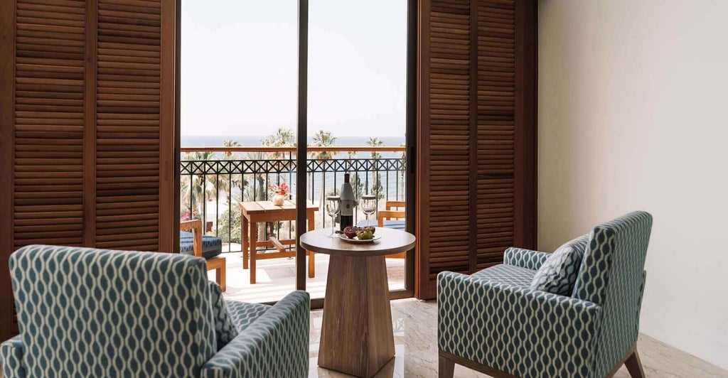 Luxurious hotel room with panoramic sea view, featuring modern decor, plush bedding, and expansive windows overlooking azure Mediterranean waters in Cyprus