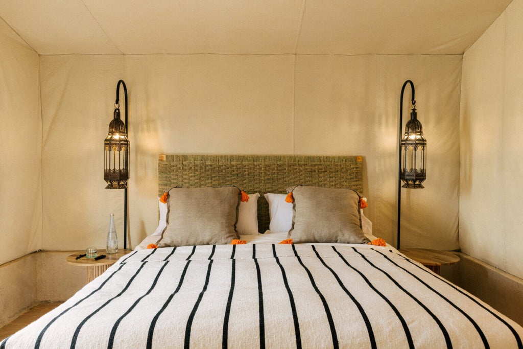 A luxurious desert tent suite featuring a king bed, canvas walls, wooden floors, and panoramic views of Morocco's Agafay desert at sunset