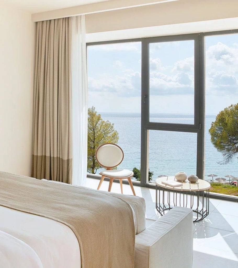 Luxurious junior suite with private hot tub, white minimalist decor, panoramic sea view, and elegant wooden accents at a scenic Greek island resort