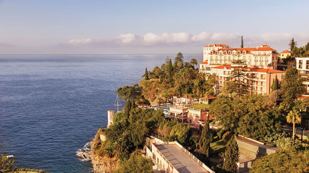 Historic luxury cliffside hotel in Madeira, featuring pink facade, lush gardens, ocean-view terraces and elegant colonial architecture