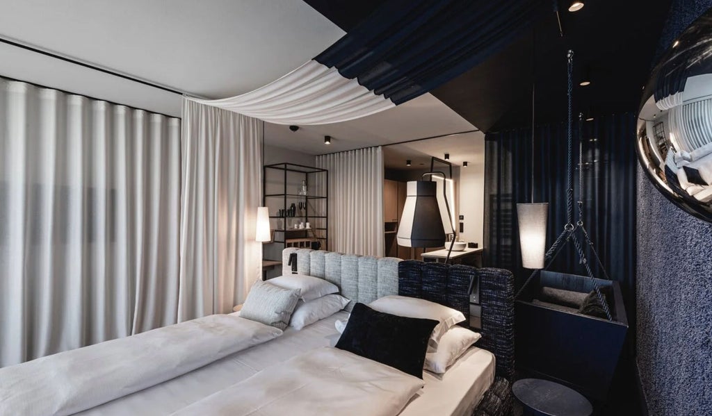 Modern boutique hotel room with plush queen bed, white linens, exposed stone walls, pendant lighting, and sleek furnishings in warm earth tones