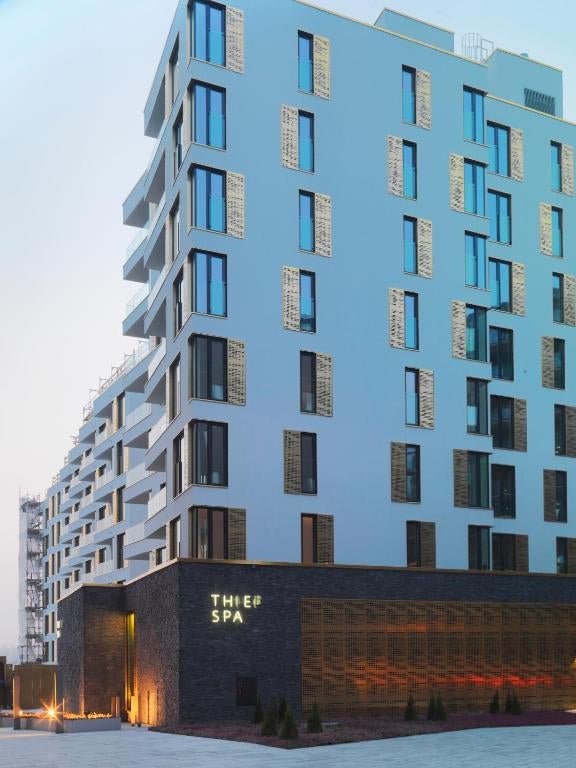 Modern luxury hotel exterior with sleek glass and metal facade, illuminated at dusk against Oslo's waterfront skyline