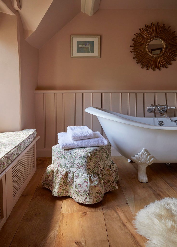 Luxurious cottage suite in UK with soft thyme-green decor, plush white bedding, and elegant rustic wooden furniture bathed in natural light