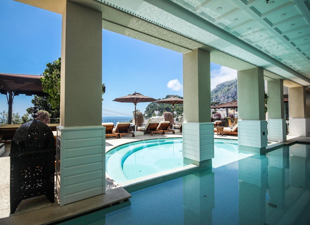 Elegant Mediterranean hotel terrace overlooking Capri's coastline, featuring infinity pool, white loungers and panoramic sea views