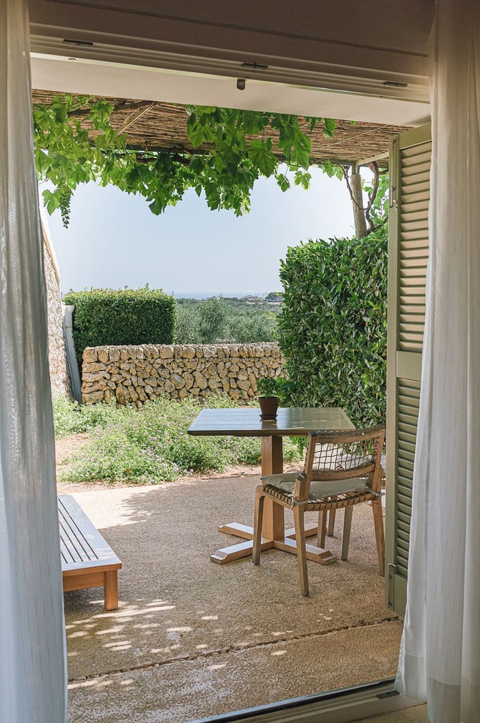 Elegant minimalist hotel room with panoramic sea view, white linens, stone walls, and modern Mediterranean design overlooking coastal scenery in Menorca, Spain