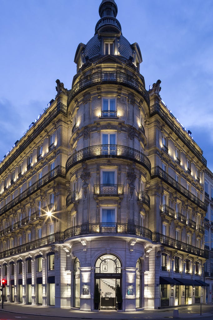 Ornate neoclassical facade of Le Royal Hotel with wrought-iron balconies, cream limestone walls, and elegant French windows at dusk