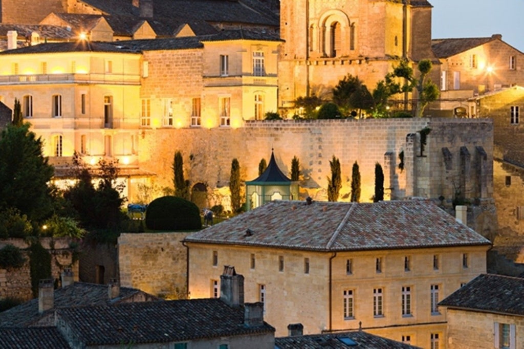 Elegant stone facade of Hotel de Pavie with ornate French windows, wrought-iron balconies, and climbing vines against warm beige walls