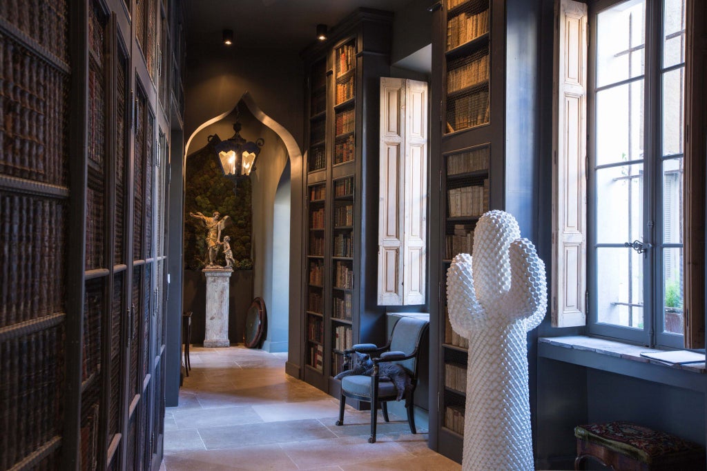 Elegant French boutique hotel facade with ornate white walls, wrought-iron balconies, and lush greenery in a historic Parisian neighborhood setting