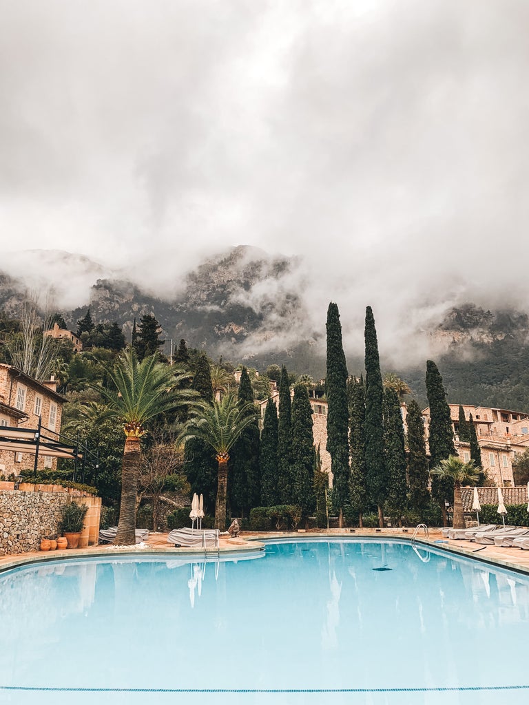 Luxurious Mediterranean hillside hotel with stone facade, arched windows and flowering bougainvillea overlooking Mallorca's countryside