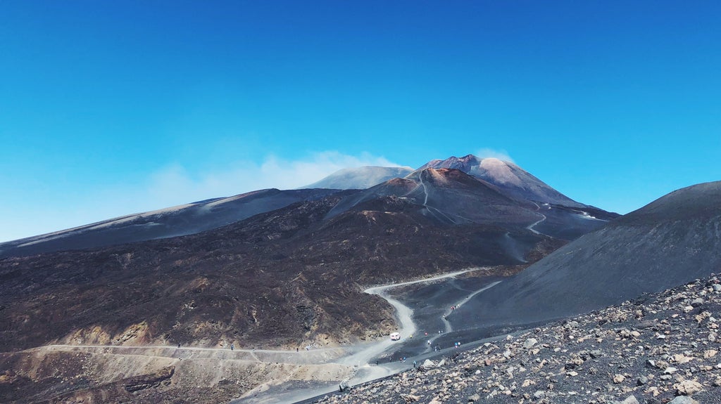 Red Jeep Wrangler traversing rugged volcanic terrain on Mount Etna, with steam vents and black lava rocks against cloudy skies