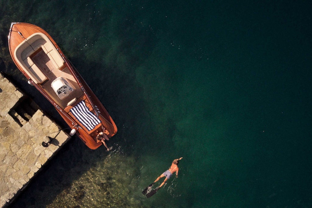 Luxury sailboat gliding through turquoise waters of Kotor Bay, Montenegro, with historic coastal town and dramatic mountain backdrop at golden hour