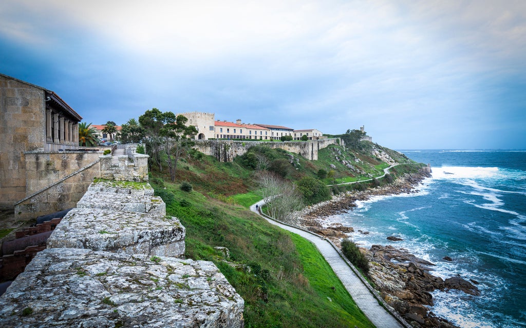 Historic stone fortress-hotel perched on rocky peninsula overlooking Bay of Baiona, with manicured gardens and medieval architecture