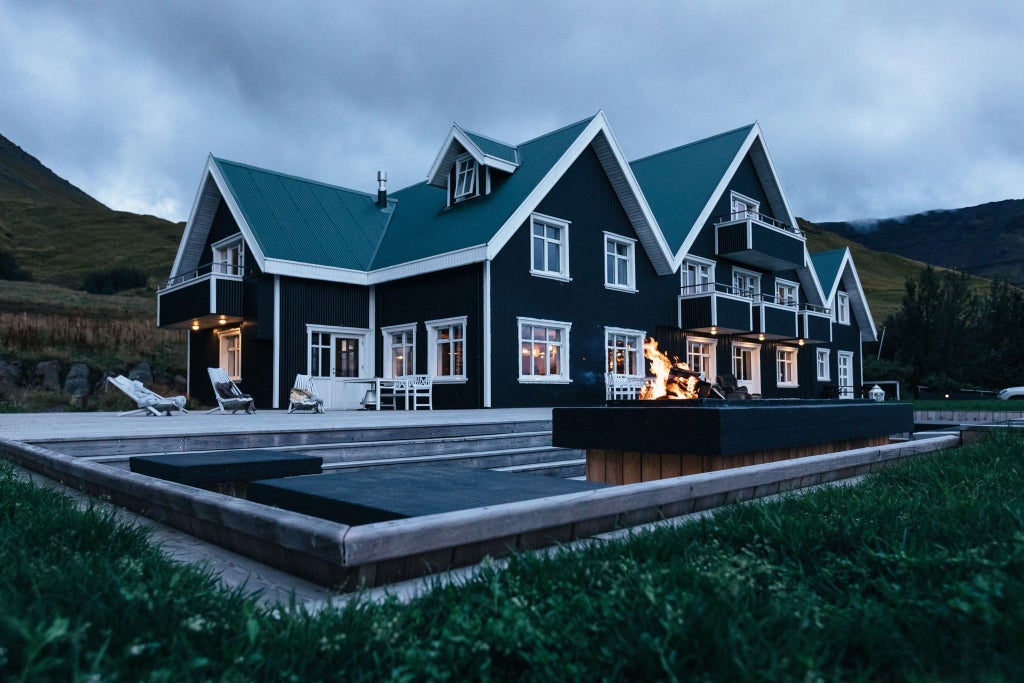 Modern Nordic boutique hotel with floor-to-ceiling windows reflecting snowy mountains, set against dramatic Icelandic landscape at sunset