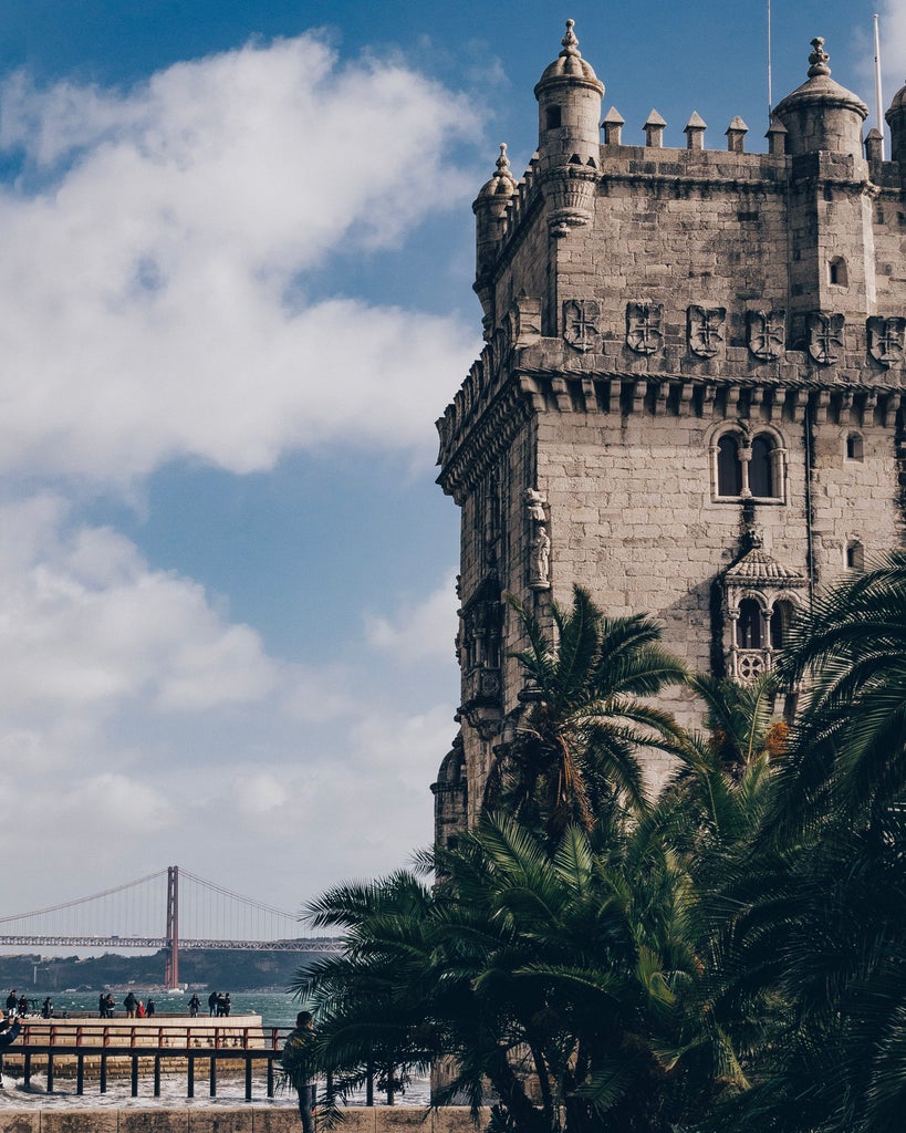 Elegant cobblestone streets of Belém, ornate Portuguese architecture, pastel-colored buildings, and a glimpse of Torre de Belém's historic silhouette against golden sunlight