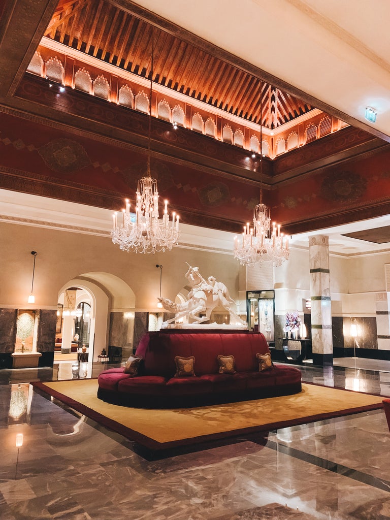 Elegant Moroccan palace hotel with ornate archways, geometric tiles, and reflective pool surrounded by manicured gardens and palm trees