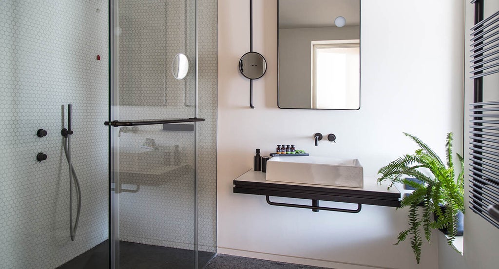 Luxurious hotel suite featuring a modern black marble bathroom, minimalist decor, and floor-to-ceiling windows overlooking Athens cityscape