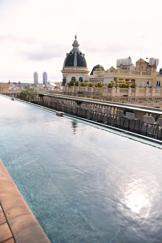 Luxurious rooftop pool overlooking Barcelona's historic skyline, with sleek modern architecture and vibrant Mediterranean design at scenset Hotel