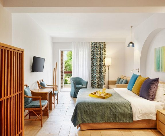 Luxurious junior suite at Eagles Palace hotel in Greece, featuring elegant white decor, private balcony with panoramic blue Aegean Sea view and modern amenities