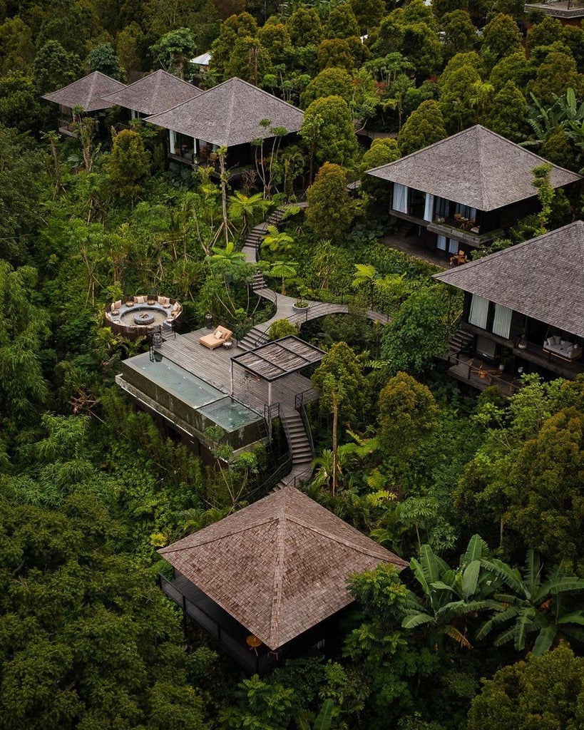 Elegant wooden cabin with floor-to-ceiling windows perched on jungle hillside, infinity pool overlooking misty Balinese mountains at sunset