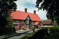 Elegant stone country hotel with thatched roof nestled in lush UK countryside, warm lighting glowing from windows at twilight