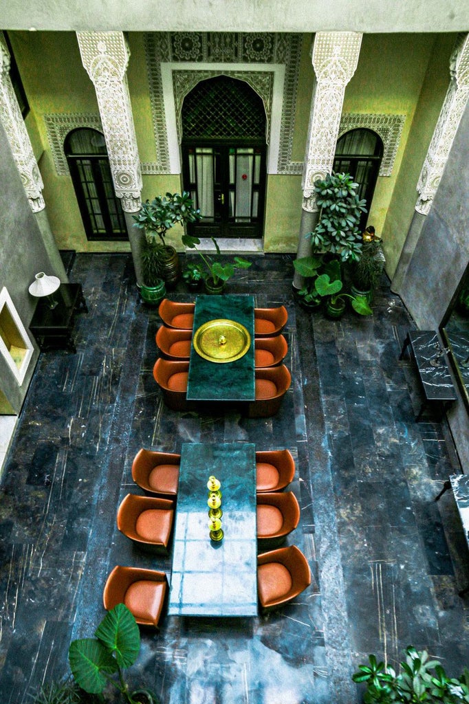 Ornate Moroccan riad courtyard with intricate blue zellige tiles, traditional archways, lush plants, and elegant fountains under soft golden light.