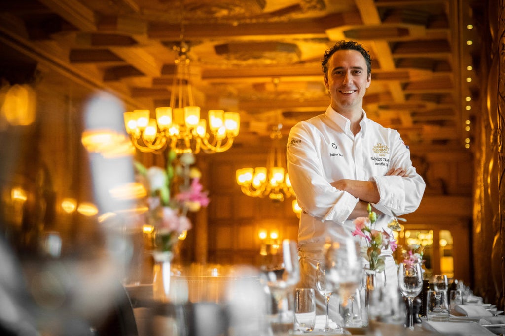 Historic luxury alpine hotel with stone facade and peaked roofs nestled in snowy Swiss mountains, surrounded by pine forest