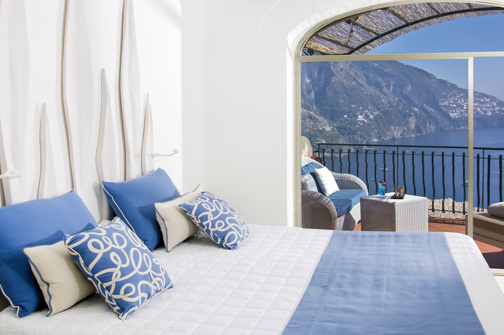 Elegant junior suite with sea-view balcony, featuring white decor, king bed, marble floors and panoramic Mediterranean vistas in Positano