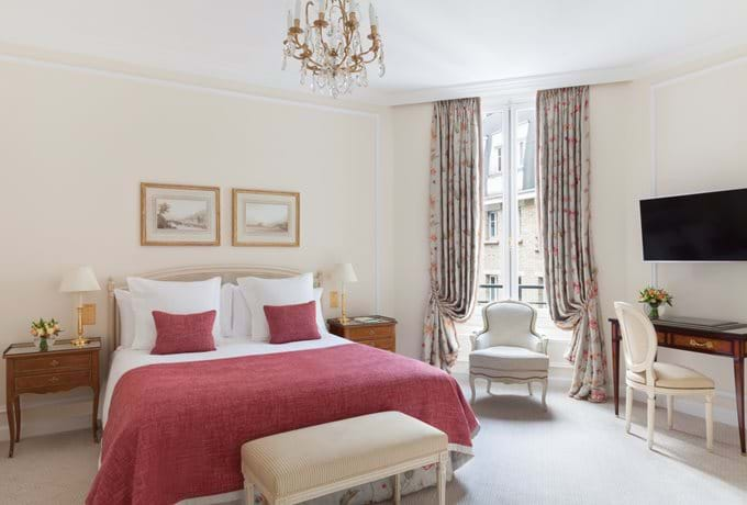 Elegant French hotel room with crystal chandelier, herringbone hardwood floors, gilded mirrors and antique furnishings in soft cream tones