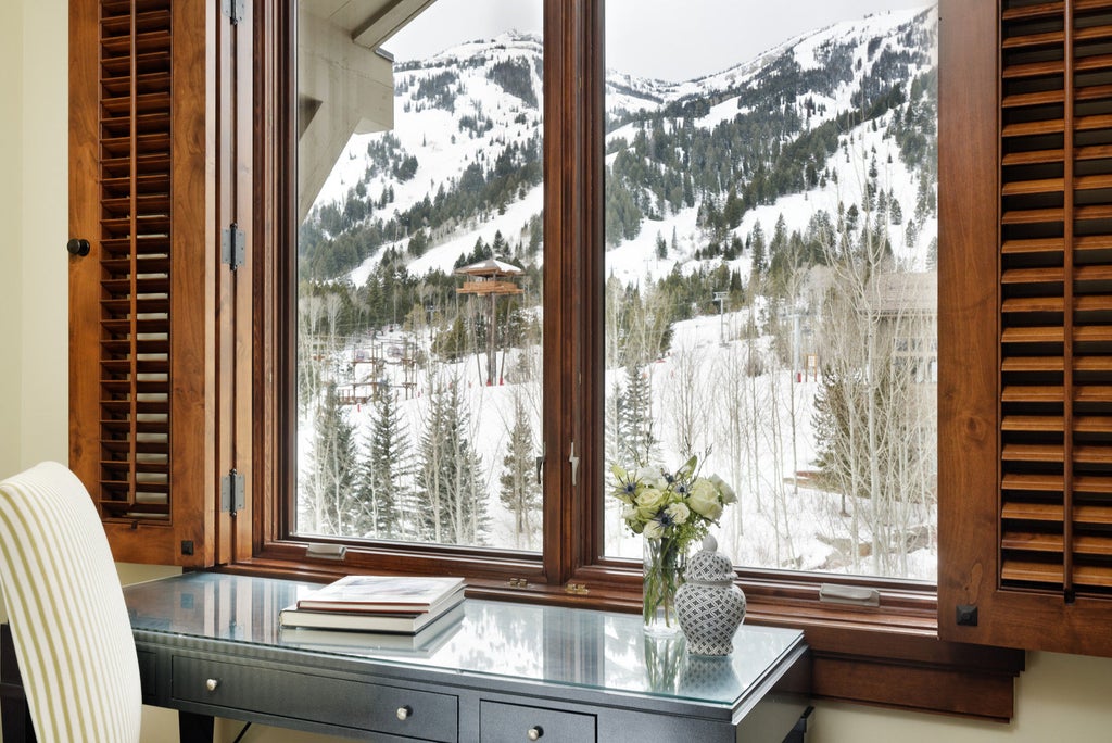 Contemporary mountain lodge with stone-and-timber facade, snow-capped peaks backdrop, luxury ski resort balconies overlooking pine forest