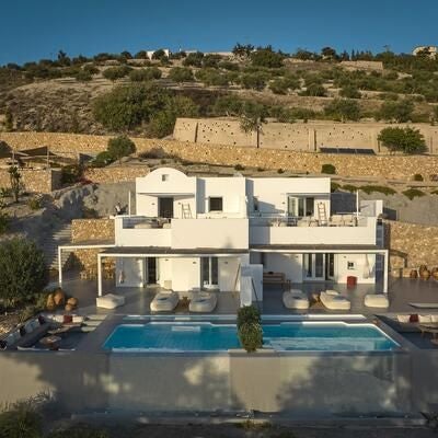 Luxurious white-washed Cycladic hotel nestled on Santorini's cliffside, overlooking azure Aegean Sea with iconic blue-domed architecture and pristine infinity pool