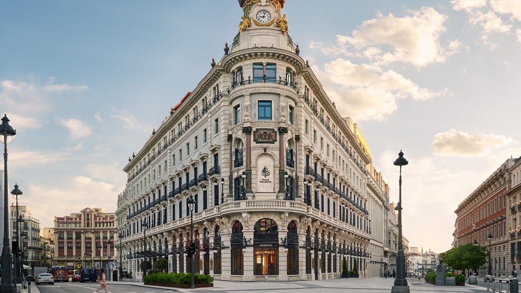 Grand neoclassical facade of Four Seasons Madrid hotel with ornate stone columns, arched windows, and elegant balconies at golden hour