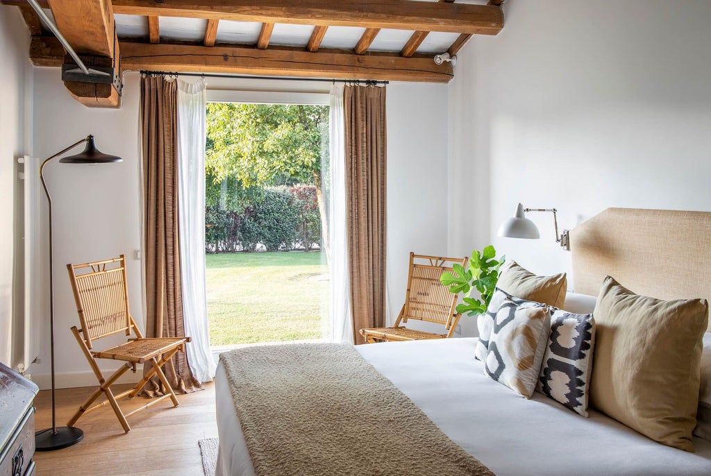 Elegant Tuscan-style suite with plush white bed, antique wooden furniture, soft neutral tones, and large arched window overlooking scenic Italian landscape