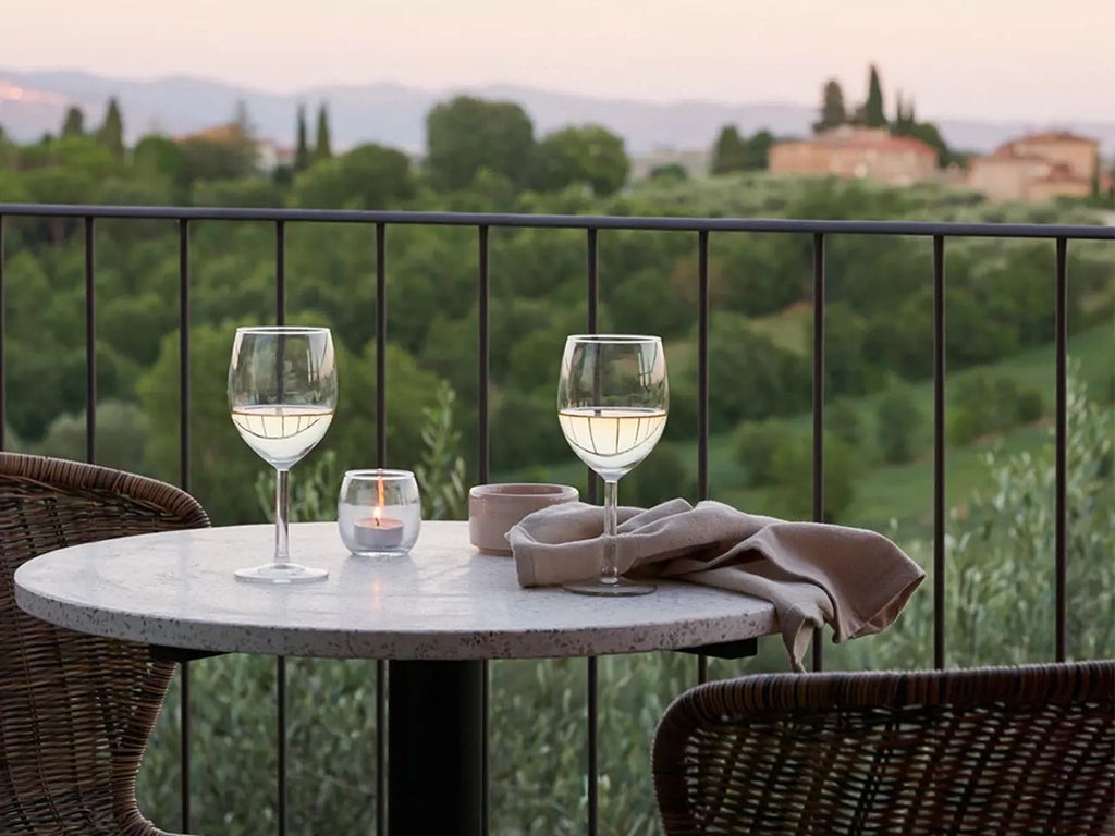 Luxurious rustic Italian boutique hotel with stone facade, terracotta roof, and elegant cypress trees against scenic Tuscan landscape at golden hour