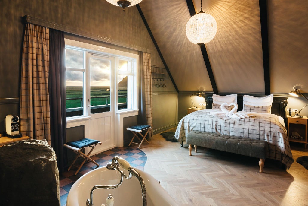 Elegant mini suite at Skálakot Manor Hotel, featuring plush white bedding, modern wood furnishings, and panoramic Icelandic landscape views through large windows.