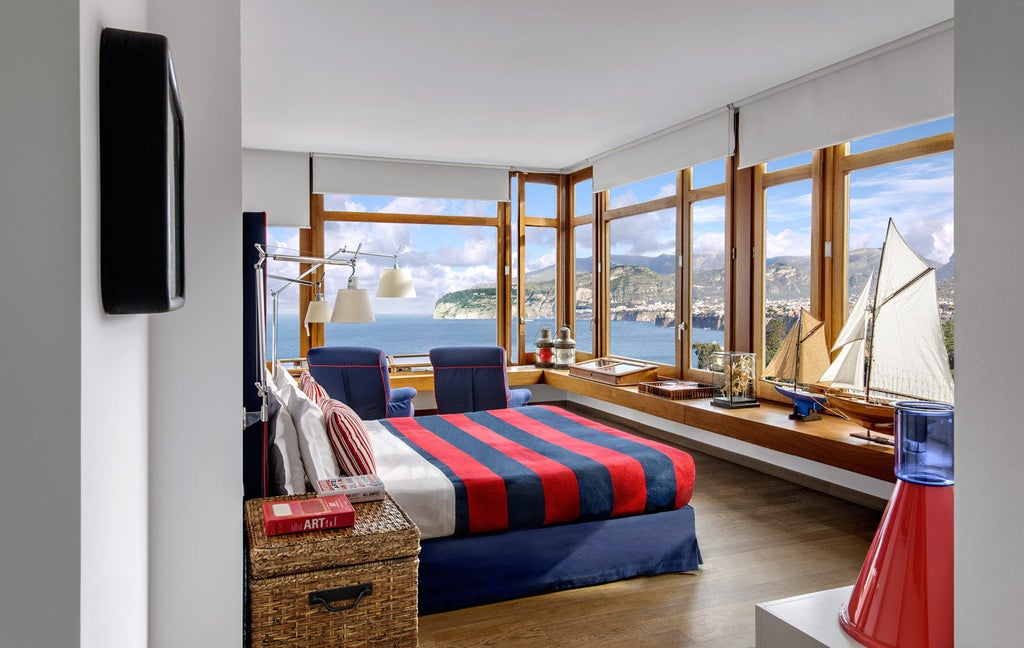 Sleek Mediterranean hotel suite with panoramic Sorrento coastline views, featuring modern nautical decor and floor-to-ceiling windows