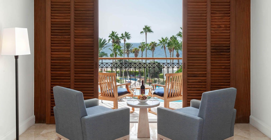 Spacious sea view room at a luxury Cyprus hotel, featuring modern white decor, plush bed, and panoramic azure Mediterranean coastline through large windows