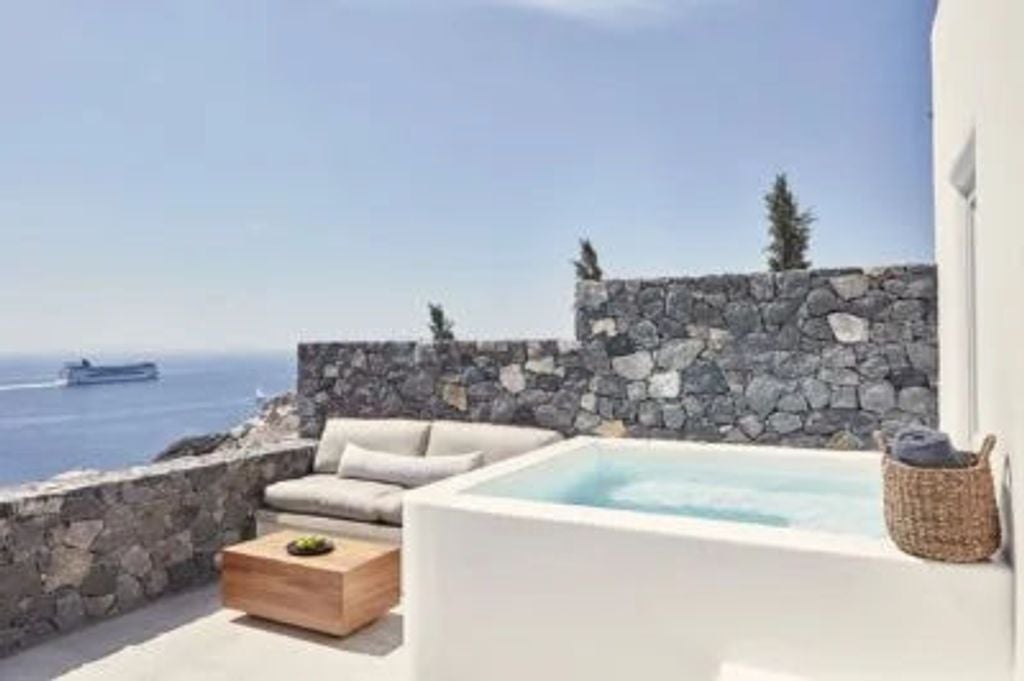 Luxurious infinity pool overlooking Santorini's azure sea at sunset, with minimalist white architecture and private cabanas