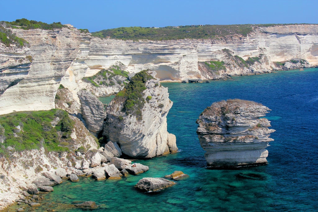 Rugged cliffs and pristine turquoise waters meet at Corsica's coastline, with a luxury yacht anchored in a secluded Mediterranean cove