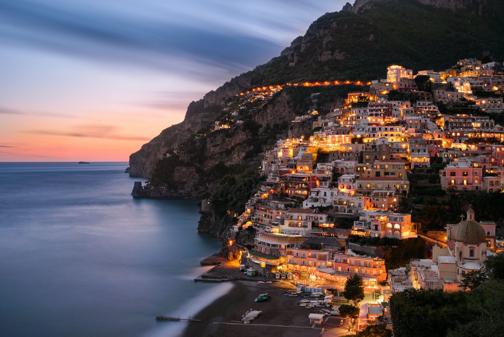 Coastal cliffs dotted with pastel villas cascade down to turquoise Mediterranean waters along Italy's scenic Amalfi Coast at sunset