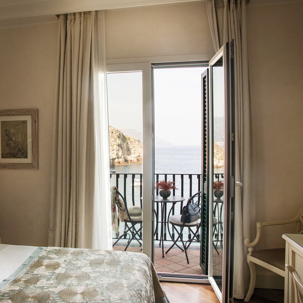 Elegant Mediterranean hotel room with white linens, ornate headboard, and terrace overlooking Taormina's crystalline bay waters