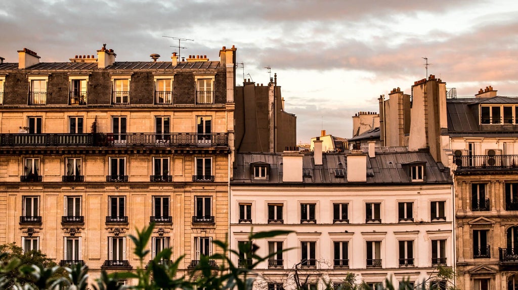 Elegant Parisian hotel facade with ornate balconies, classic French architectural details, and lush greenery framing historic urban streetscape