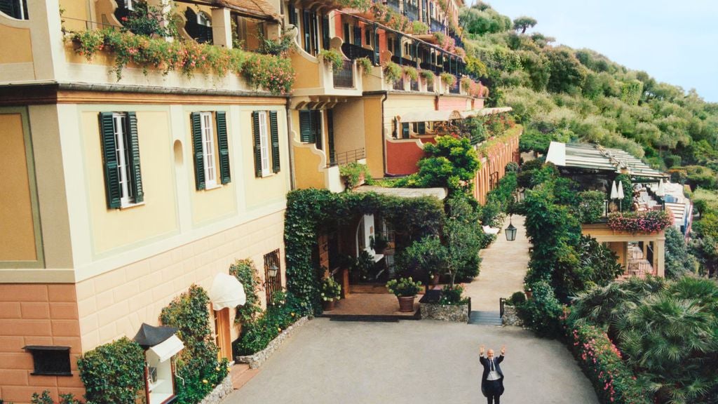 Elegant Mediterranean hotel with terraced gardens overlooking Amalfi Coast, white facade adorned with climbing vines and arched windows