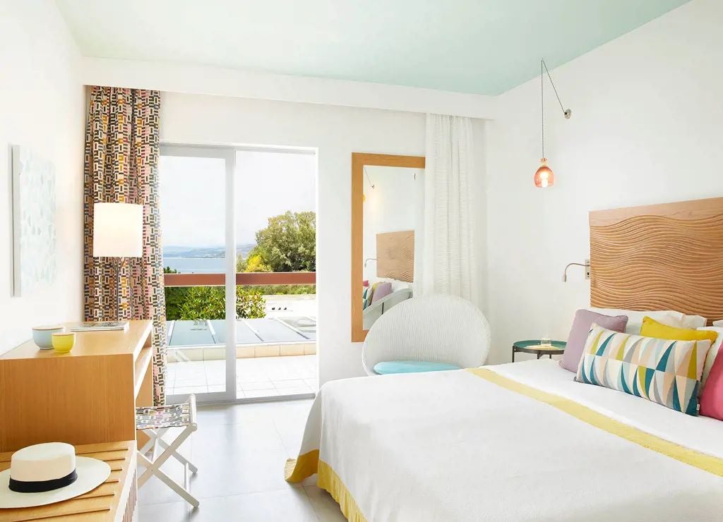 Elegant double room with garden view at Eagles Palace hotel, featuring luxurious white linens, wooden furnishings, and Greek coastal landscape through large windows