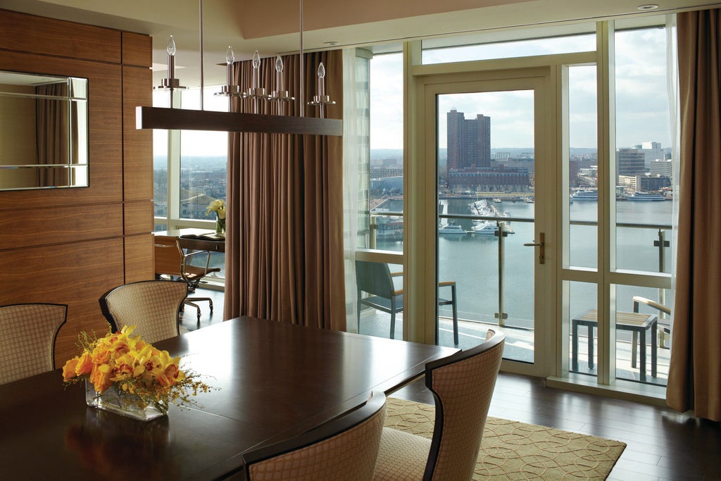 Elegant glass skyscraper hotel overlooking Baltimore's Inner Harbor with waterfront promenade, infinity pool, and private balconies at sunset