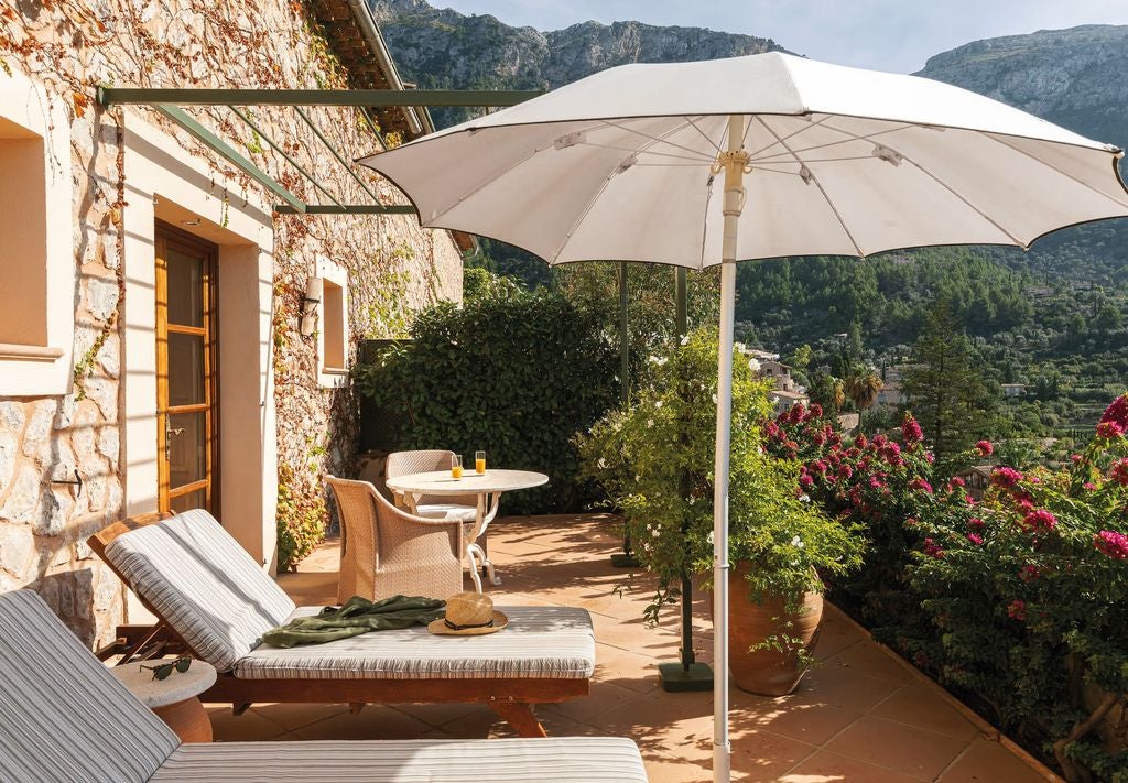 Elegant junior suite with terracotta floors, white walls, wooden beams, plush king bed, and traditional Mallorcan furniture in rustic-luxe style