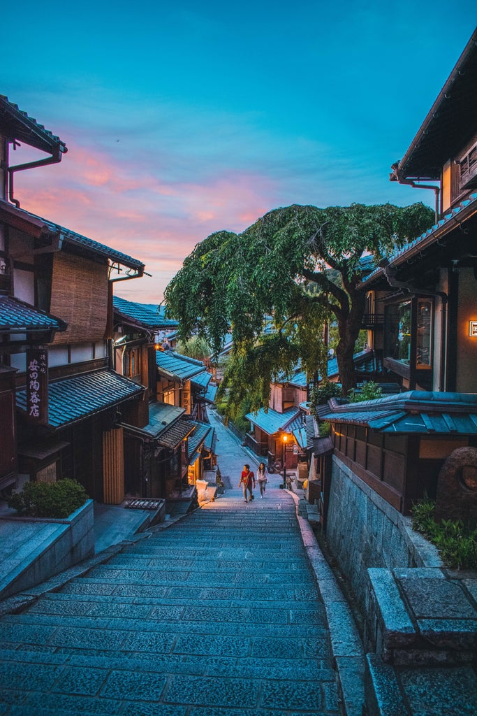 Traditional Japanese temple gate with glowing red lanterns at dusk, nestled among manicured gardens and illuminated maple trees