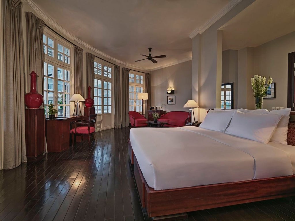 Elegant colonial-style suite with antique wooden furnishings, soft cream walls, French windows overlooking lush gardens at scenset resort in Hue, Vietnam