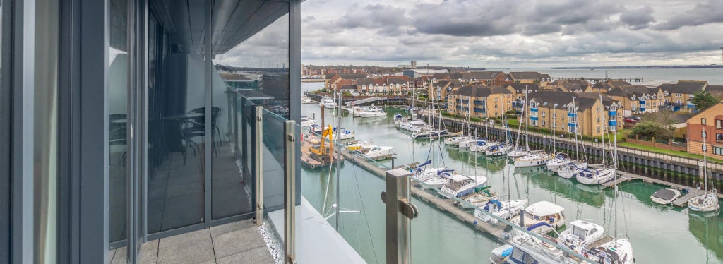 Elegant double room with Juliet balcony overlooking scenic harbour, featuring plush bedding, modern decor, and warm lighting in a sophisticated Southampton hotel