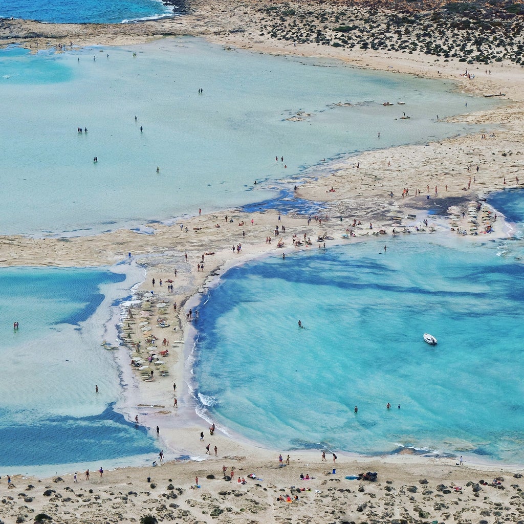 Tranquil turquoise waters of Mediterranean Sea meet white sandy beach, framed by rugged cliffs and traditional Greek architecture in Crete